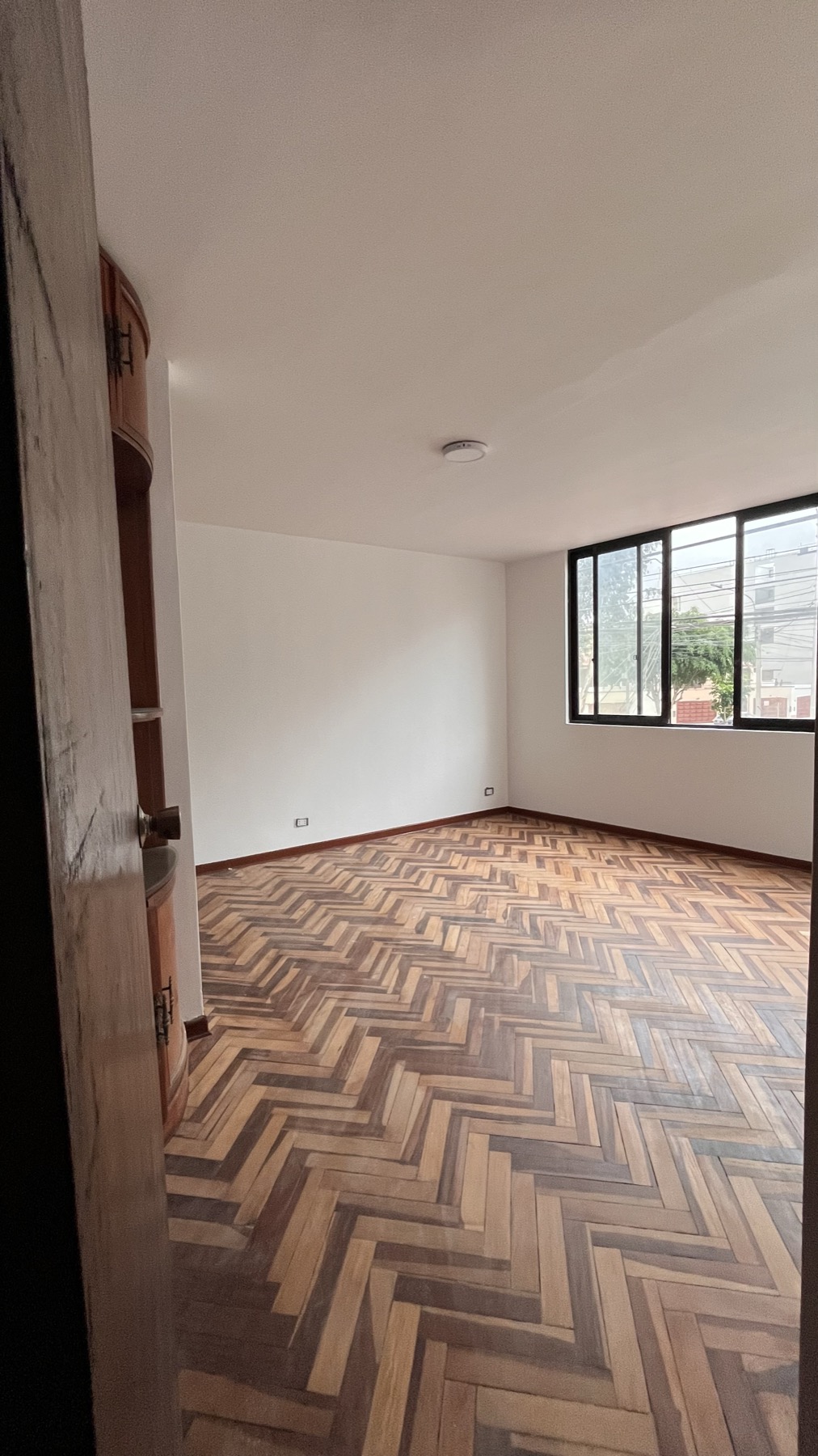 Sala principal de la oficina en alquiler en Surco con piso de parquet y ventana de esquina