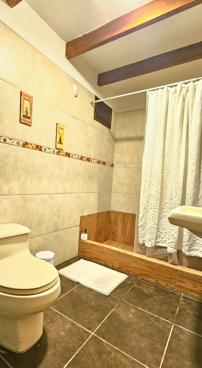 Baño con ducha, vigas de madera y piso de porcelanato